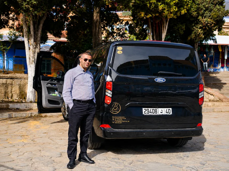 Private driver beside the black transfer van in Chefchaouen, loaded for the long drive to Casablanca